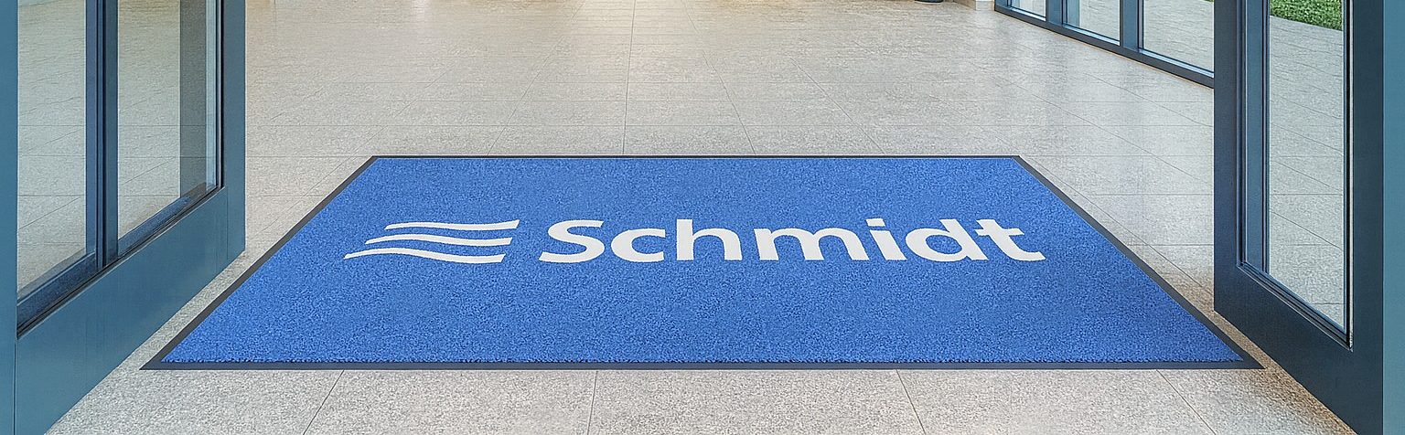 Logo-Matte mit der Aufschrift Schmidt Services in Blau im Eingang eines Bürogebäudes