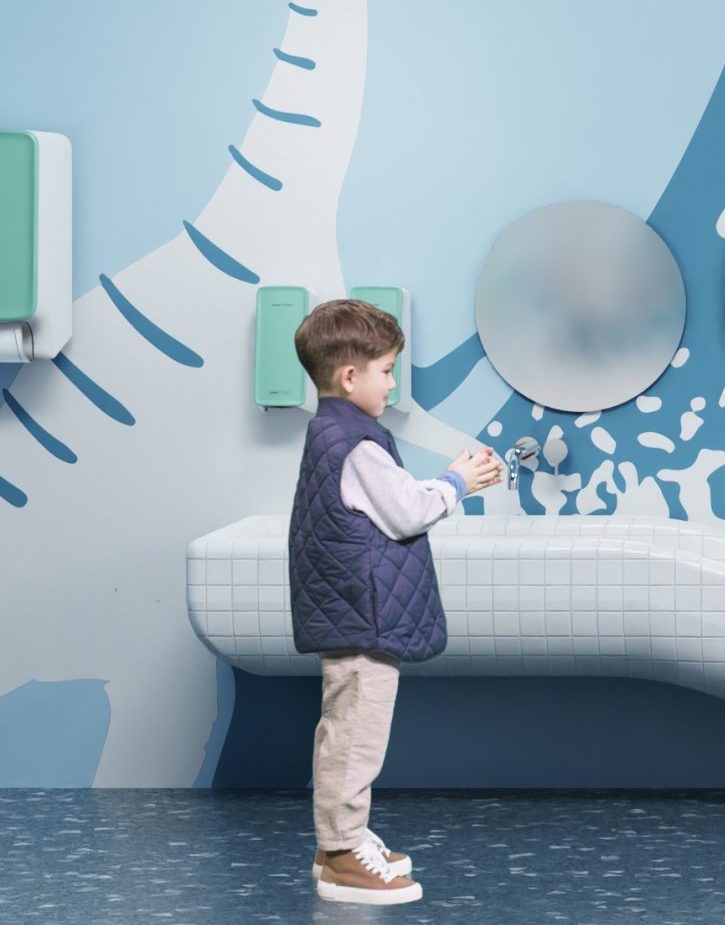 Kind in einem nachhaltigen Waschraum eines Kindergartens. PureLine Seifenschaumspender in Mint